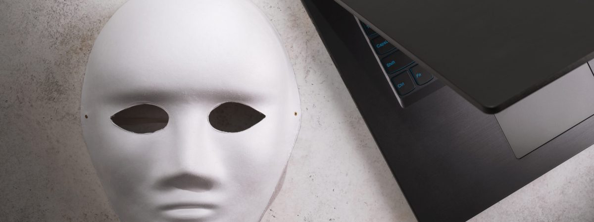 White mask and laptop on the table, top view, internet anonymity concept